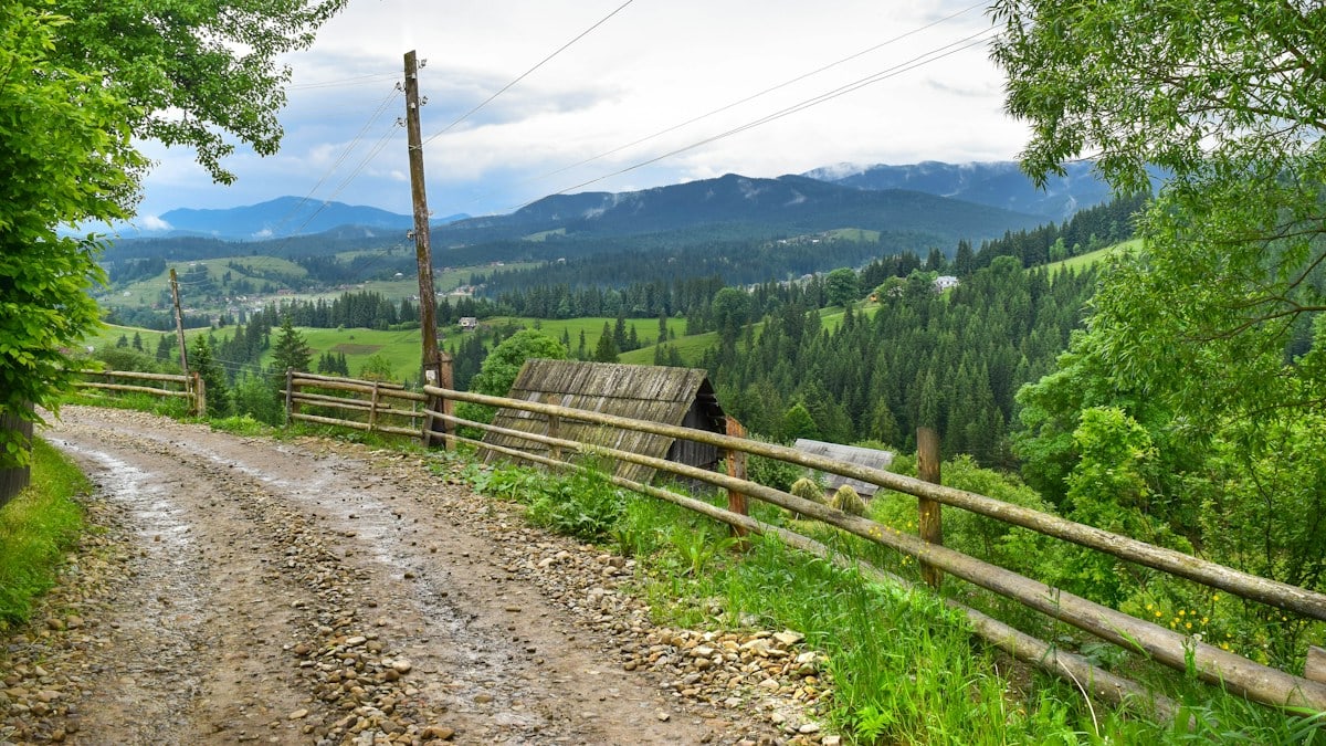 a dirt road with a wooden fence and mountains in the background